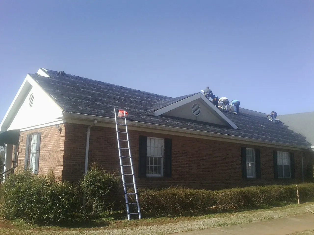 Crew tearing shingles off a brick ranch roof with a ladder set — Metal Roof Repair work by our crew in Hopedale