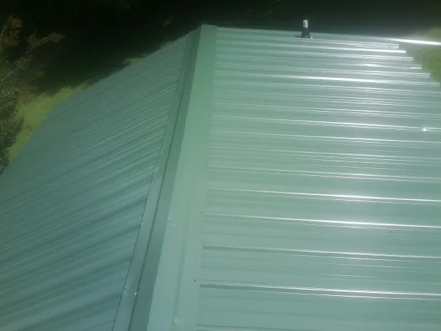 New green metal panels meeting at the ridge of a roof — Flat Roof Repair work by our crew in Hopedale