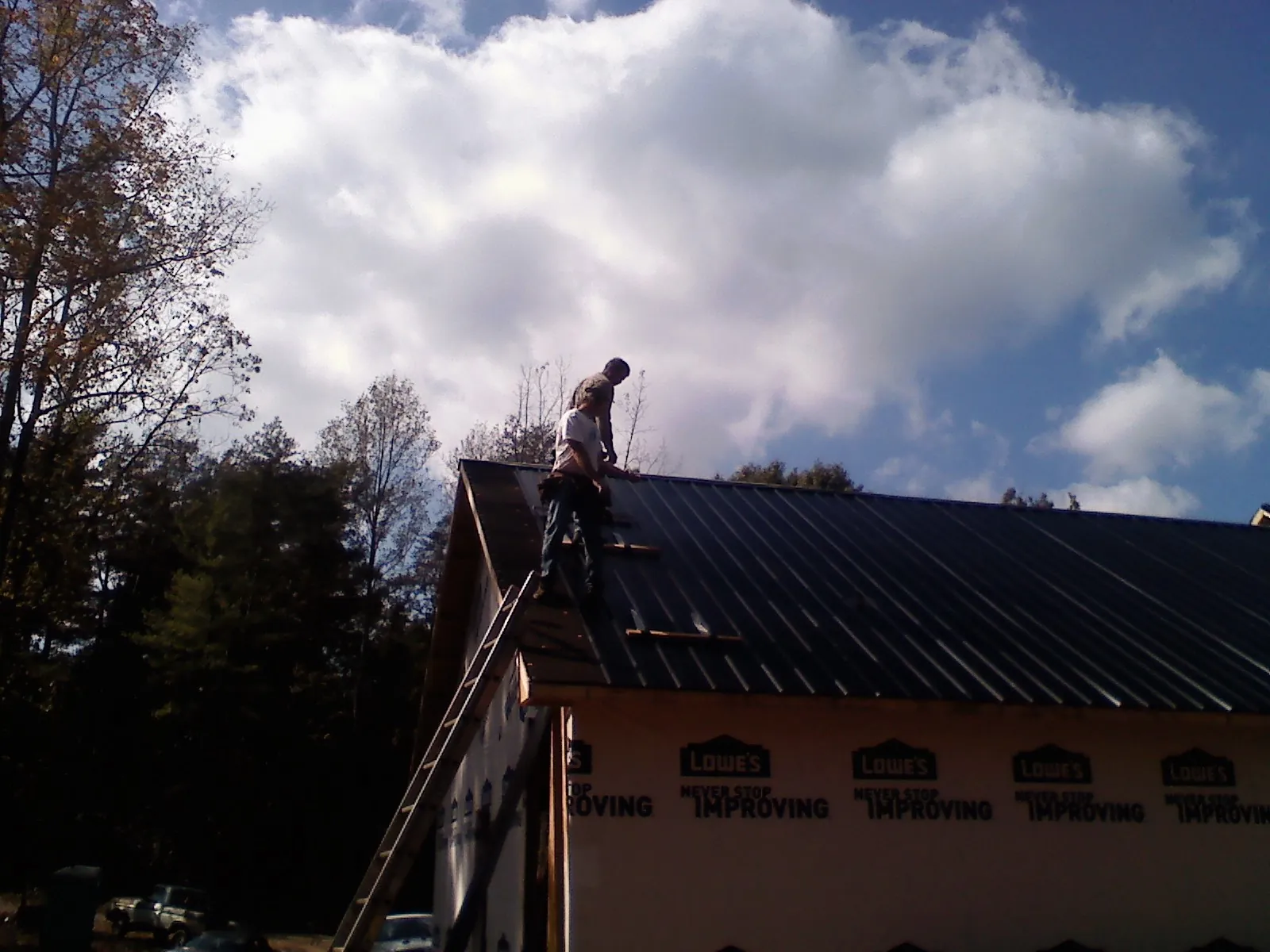 Roofer fastening dark metal panels high against a cloudy sky, from a Roof Inspection job in Hopedale