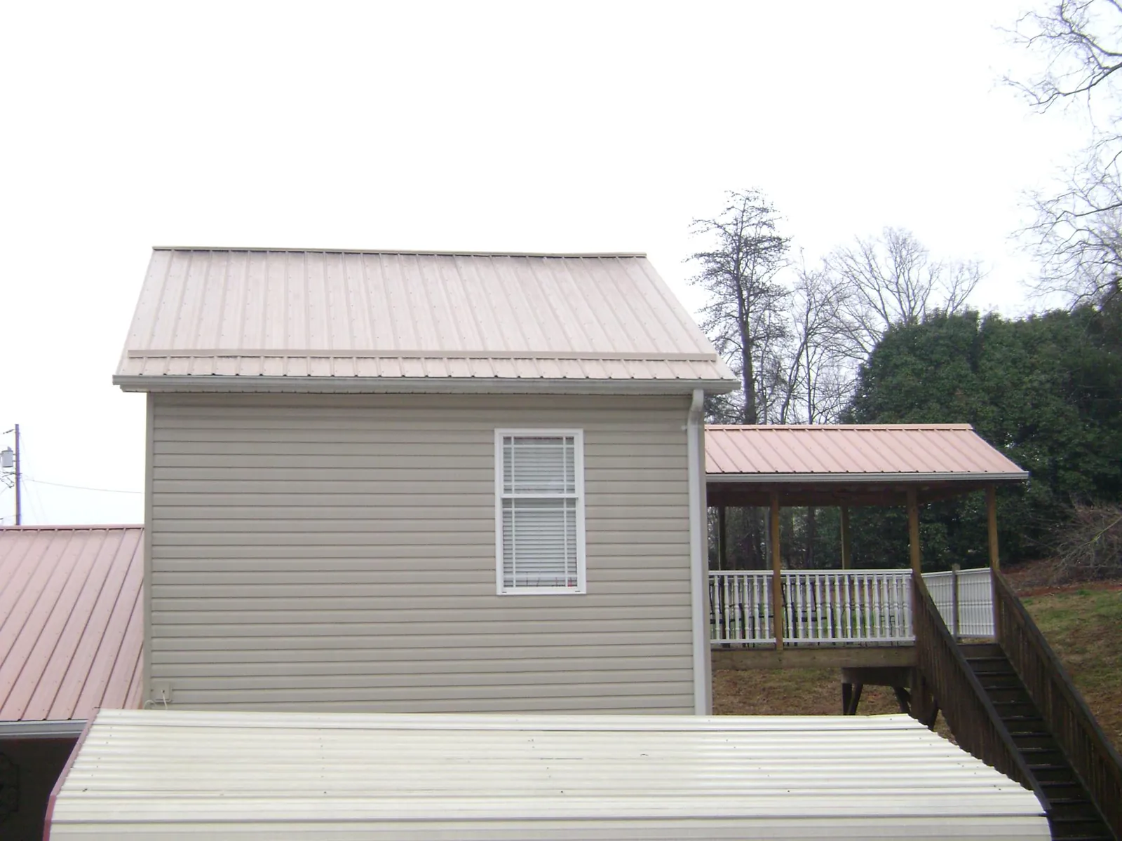 Tan metal roofs on a two story addition and attached porch, from a Roof Replacement job in Hopedale
